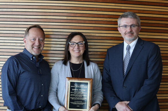 Three people pose for a photo while a woman in the middle holds an award