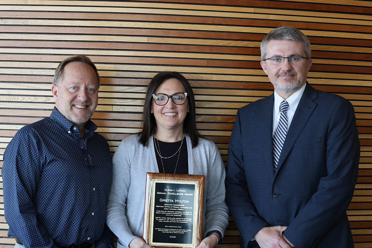 Three people pose for a photo while a woman in the middle holds an award