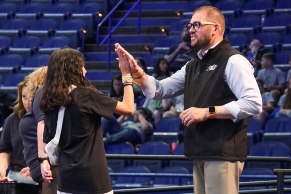 A man wearing glasses high fives a student in an arena