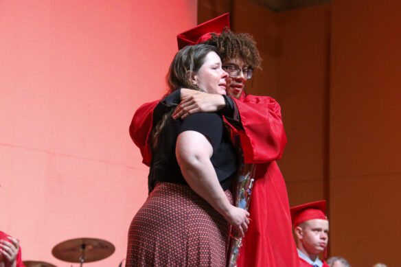 A man in a red graduation cap and gown hugs a woman