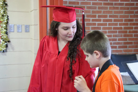 A woman in a red gap and gown looks down at a younger student