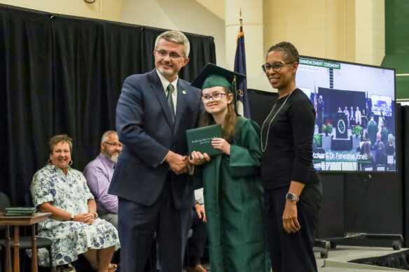 Commissioner of Education Robbie Fletcher, left, and KSD Interim Principal Faneshia Jones, right, present a diploma to graduate Mikayla Gilmore, center.