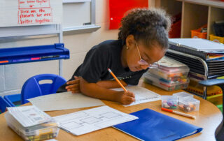 A young student sitting at a desk with a pencil in hand working on an assignmnet