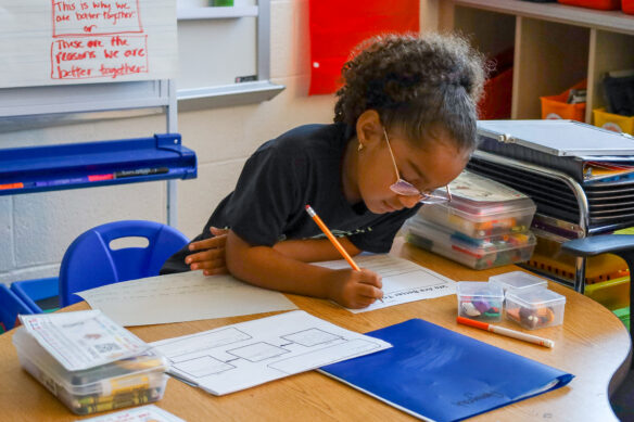 A young student sitting at a desk with a pencil in hand working on an assignmnet