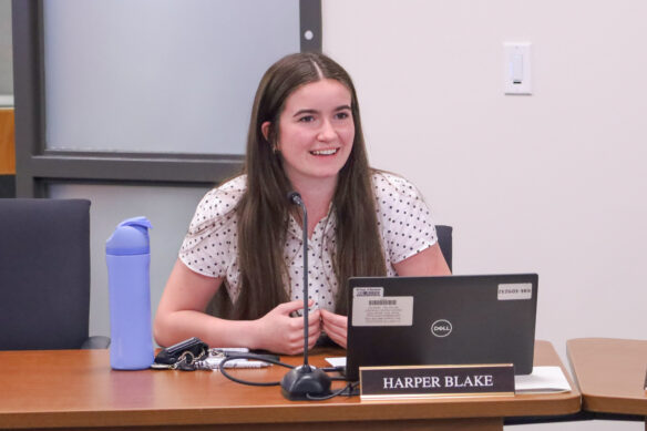 A woman sits at a table and speaks into a microphone