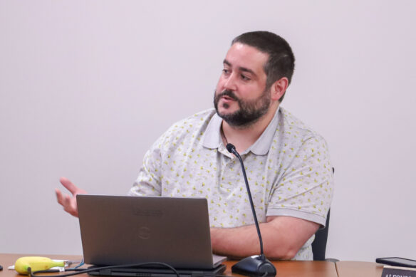 A man sits at a table and speaks into a microphone
