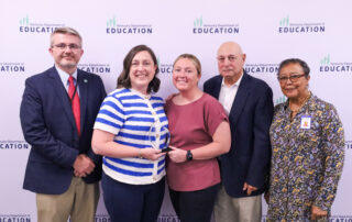 Five individuals stand in front of a background while the middle two accept an award.