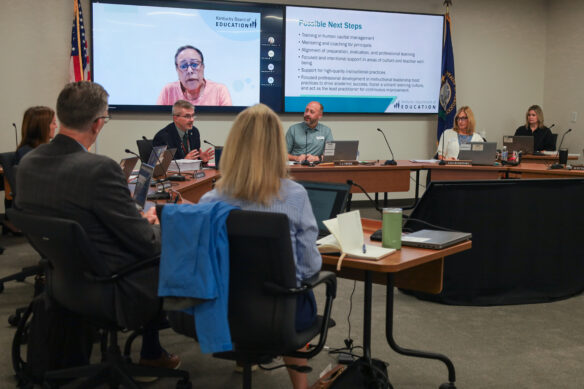 Robbie Fletcher sits in a boardroom, surrounded by a few members of the Teachers Advisory Council, speaking to them