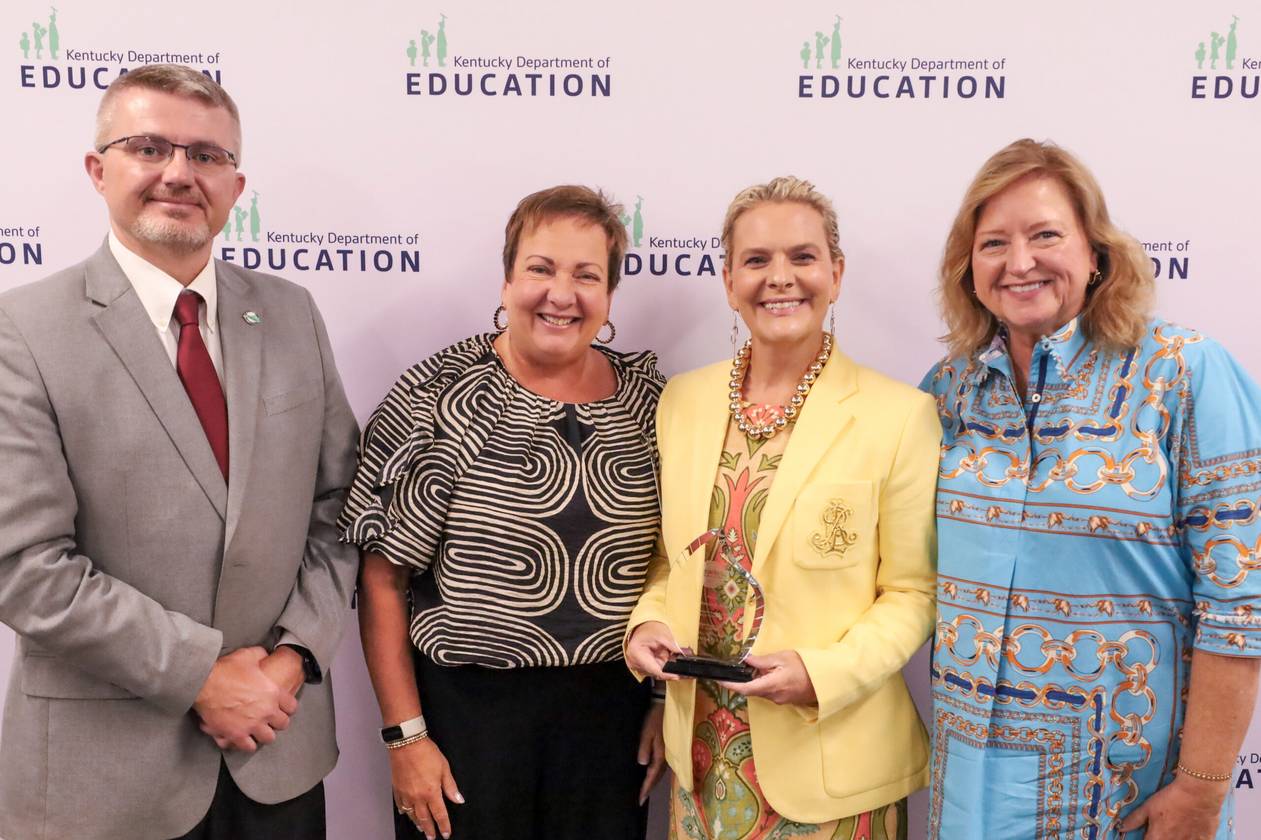 Group of four people standing in front of a white background accepting an award.