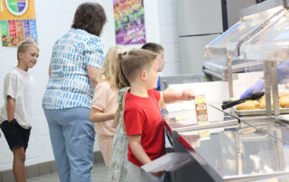 A group of young students stand in a cafeteria line waiting to pick up their lunches.
