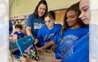 A teacher working with a group of students as they hold a tablet in front of Legos.