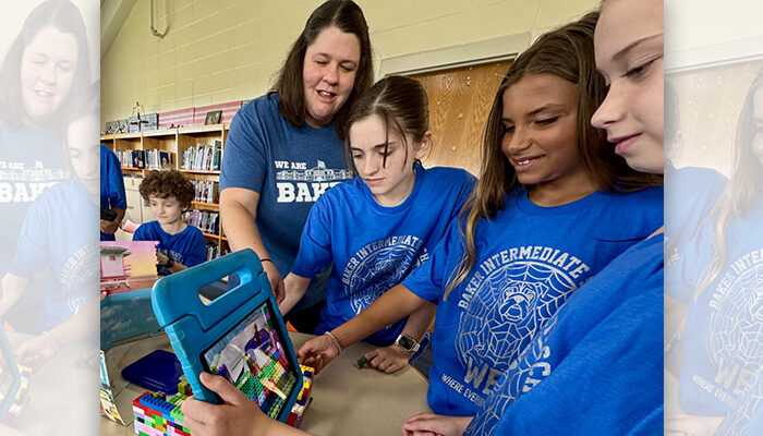 A teacher working with a group of students as they hold a tablet in front of Legos.