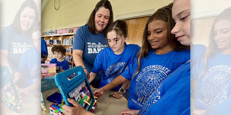 A teacher working with a group of students as they hold a tablet in front of Legos.