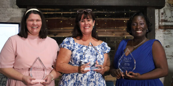 Katherine Berner, Molly Seifert and Kellie Moses hold glass trophies and smile.