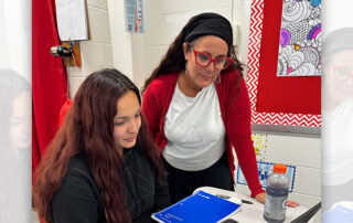 A teacher working with a student on a laptop.