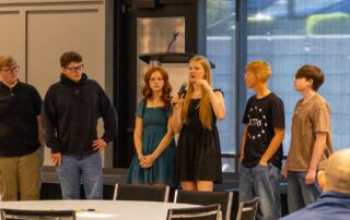 Students standing in front of a crowd speaking into a microphone