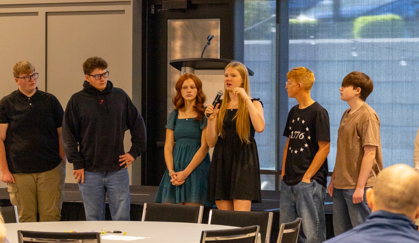 Students standing in front of a crowd speaking into a microphone