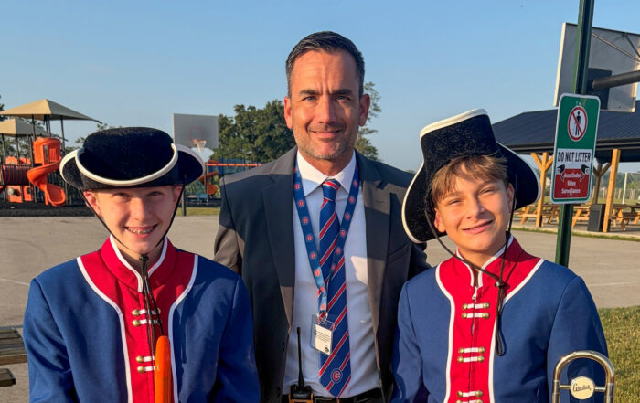 A man in a suit stands with two students in costumes