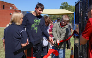 A group of kids cut a giant red ribbon in front of a metal gate