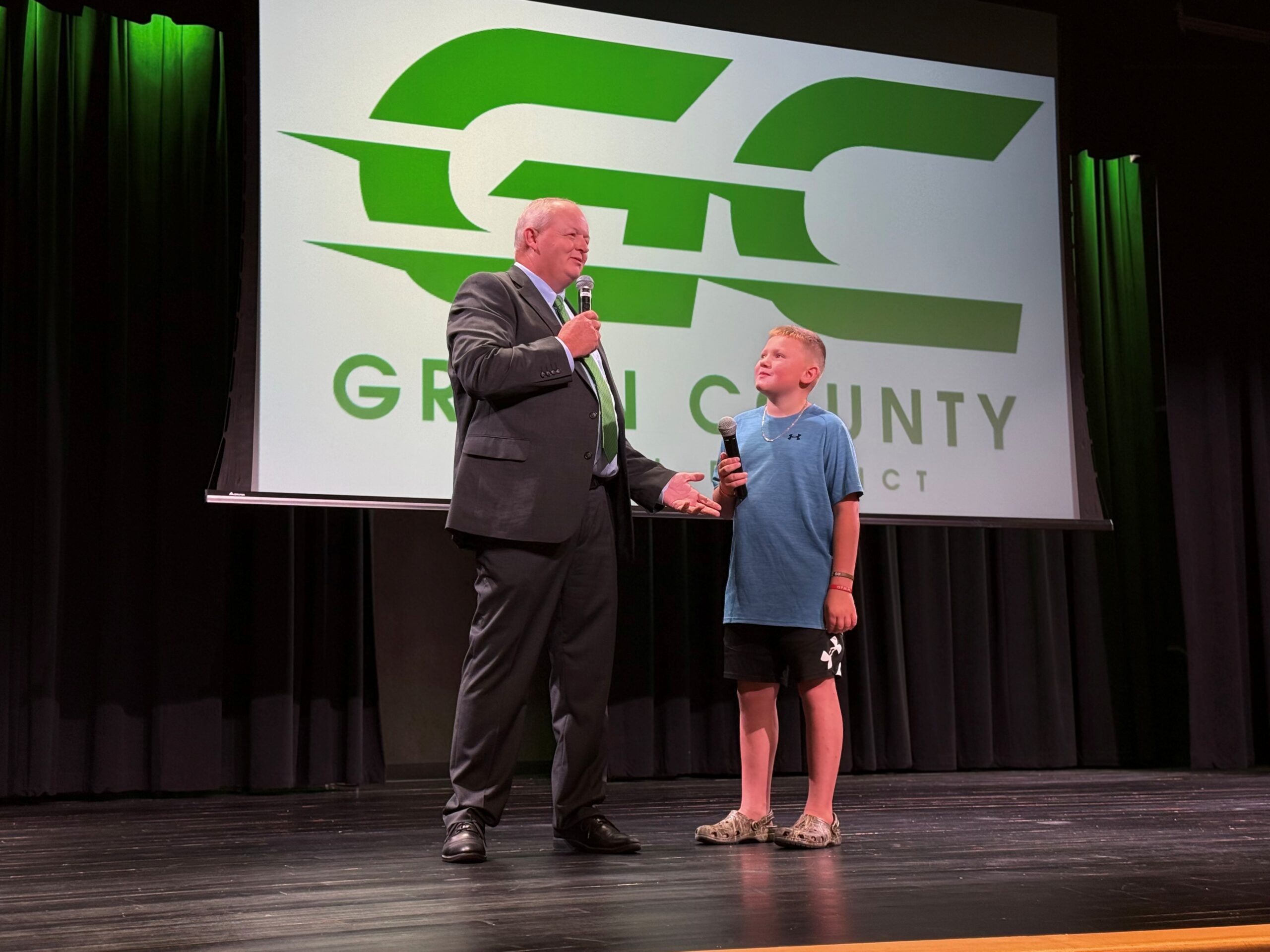 A man holds a microphone and stands on stage with a kid