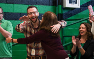 Tyler Saylor hugs a teacher while other teachers smile and clap.